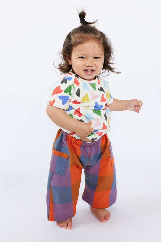 Child wearing a colorful shirt with heart pattern and multicolored pants by Lilla Barn Clothing on a white background