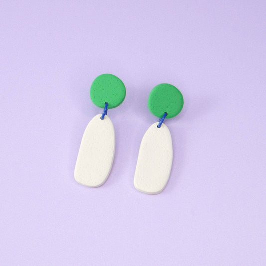 Pair of earrings with green circular tops and white oval bottoms on a purple background