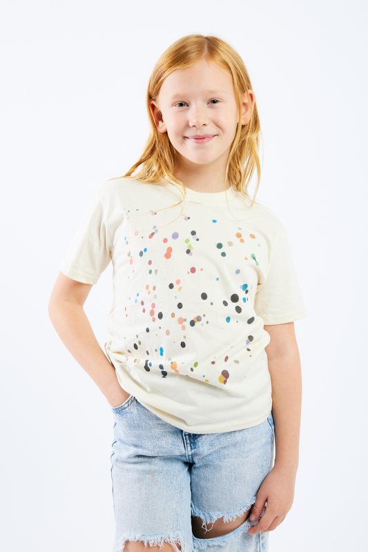 Young girl wearing a cream t-shirt with colorful polka dots and ripped jeans on a white background