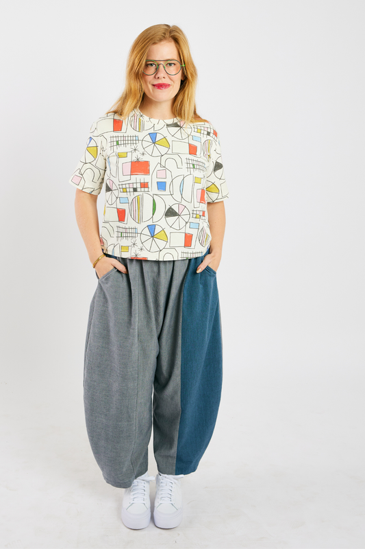 person wearing gray and blue barrel-leg pants made from sustainable bamboo and cotton. She's also wearing a colorful, organic cotton t-shirt, and glasses from Eye Spy Optical.