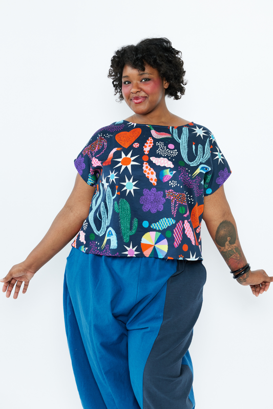 Person wearing a colorful patterned top and blue pants on a white background