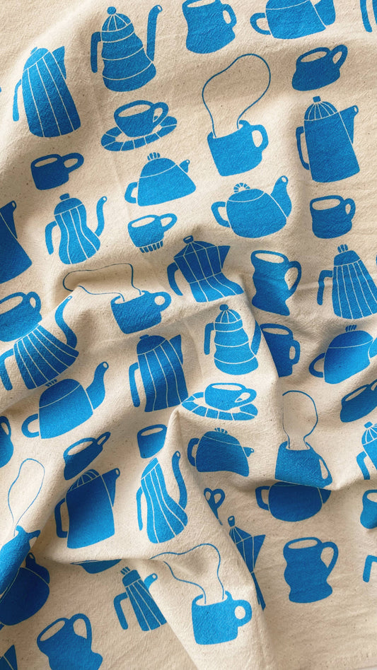 Beige cotton towel with blue tea-related illustrations including teapots, cups, and saucers.