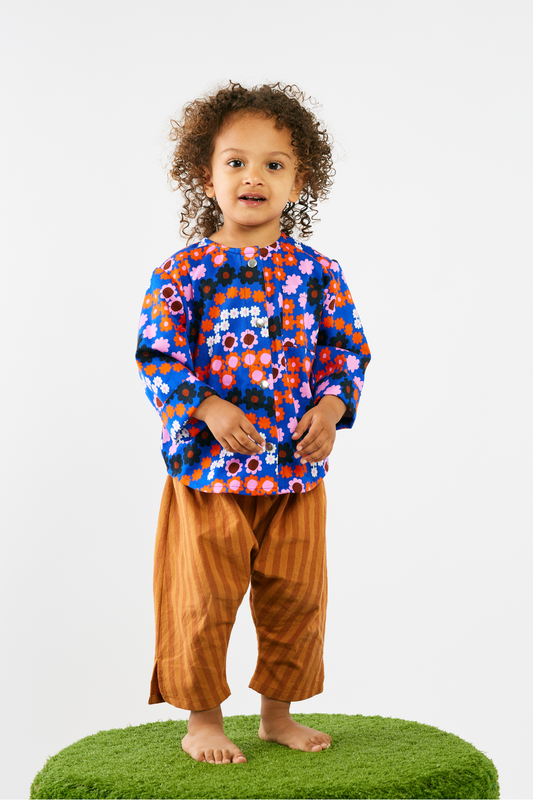 Child wearing a colorful floral shirt and brown pants on a white background