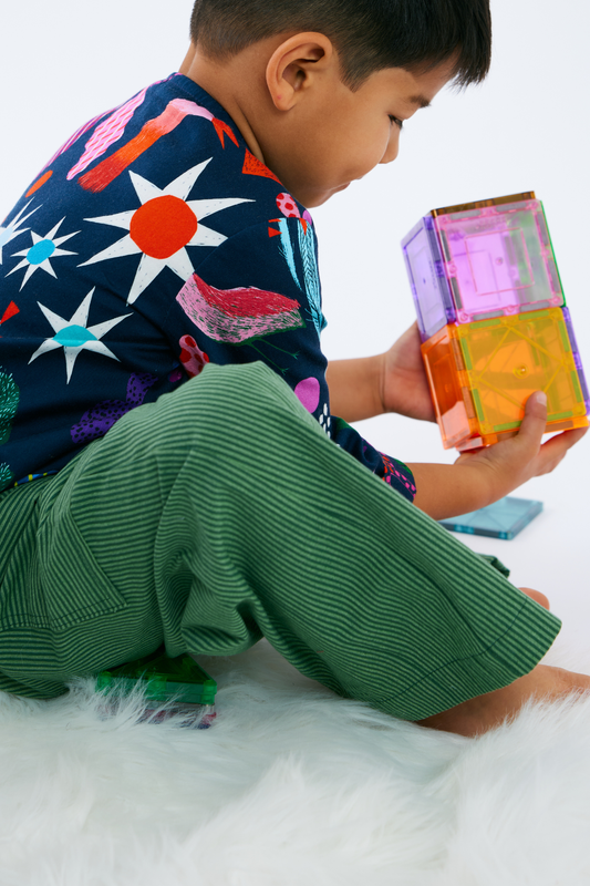 Child playing with colorful building blocks on a white surface wearing colorful green pants