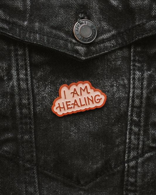 enamel pin with 'I AM HEALING' text on a black denim jacket