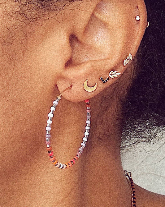 Close-up of an ear with multiple earrings including a beaded hoop earring.