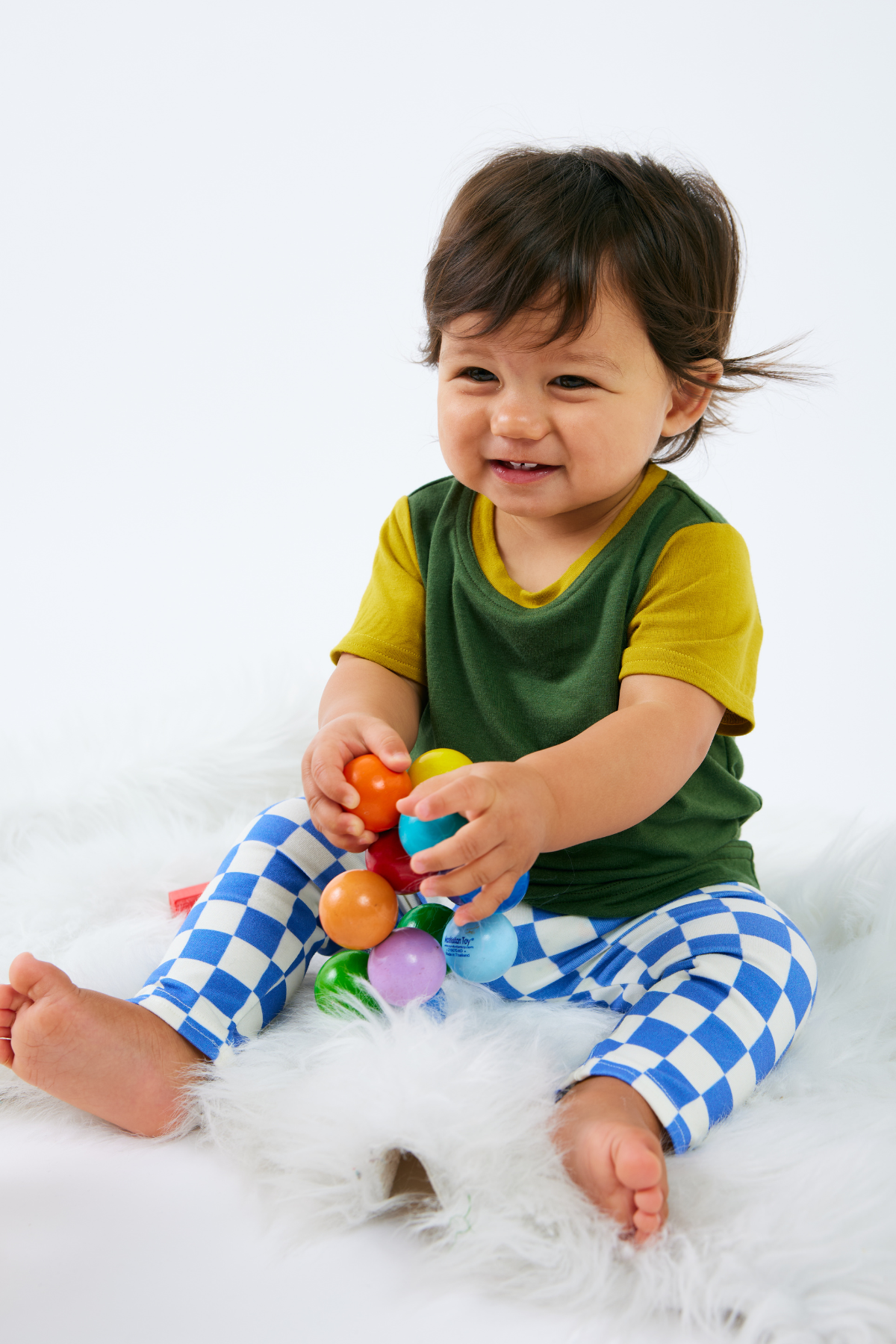 Baby wearing a green and yellow bamboo t-shirt with blue checkered organic cotton leggings, sitting on a white surface.