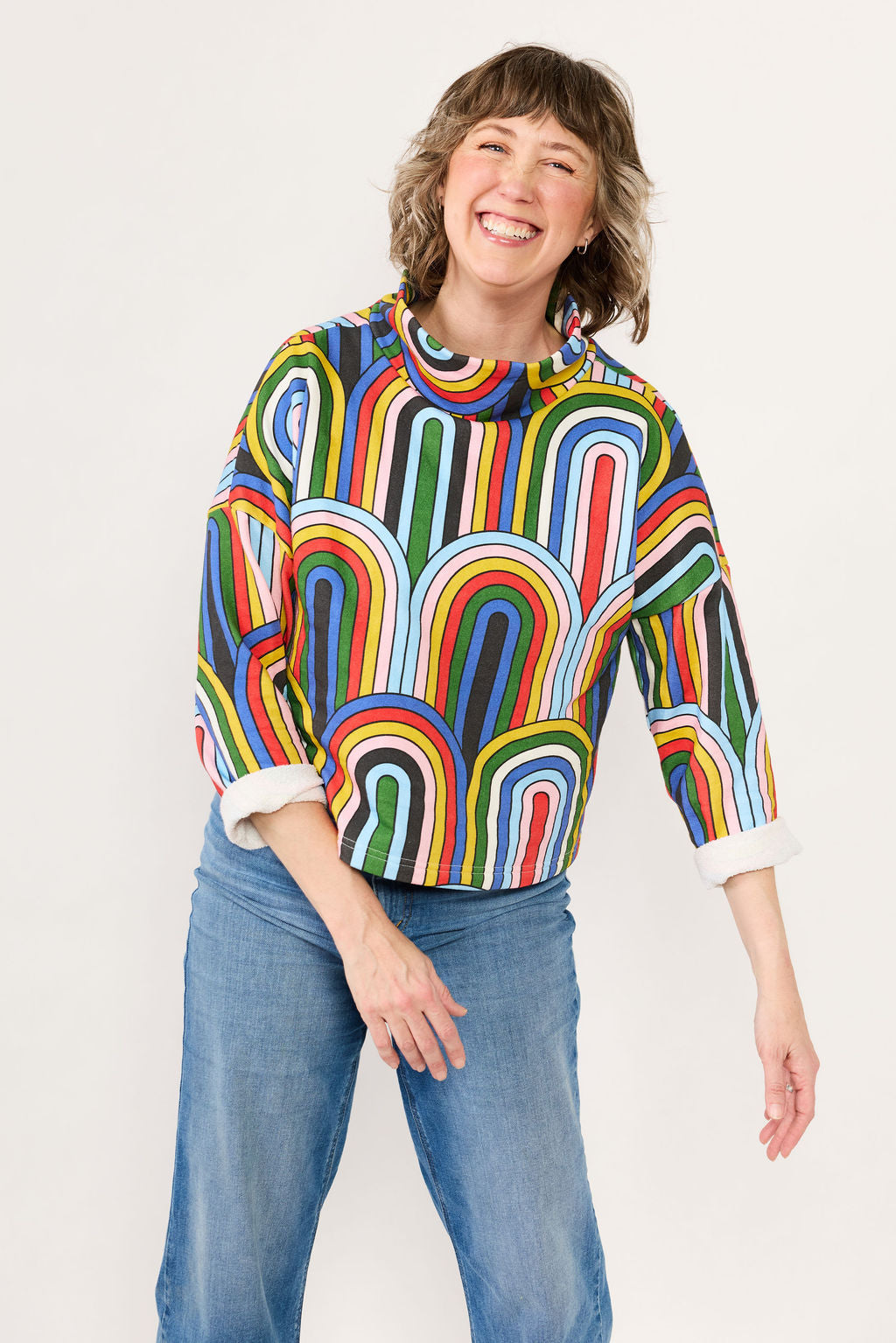 Lilla Barn Clothing owner wearing a colorful rainbow-patterned sweater against a white background