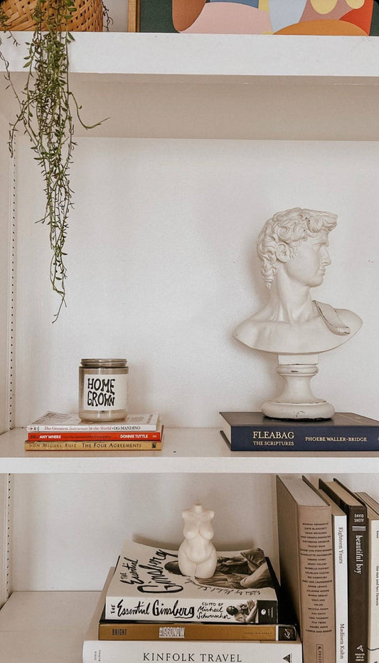 Decorative shelf with books, a candle, and a bust sculpture against a white wall.