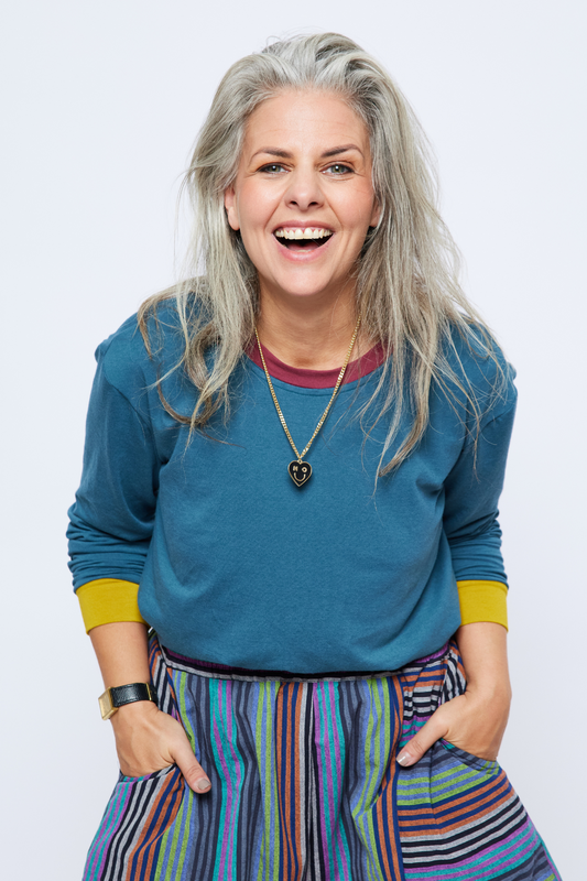 woman smiling with her hands in her pockets wearing a blue bamboo long sleeve top