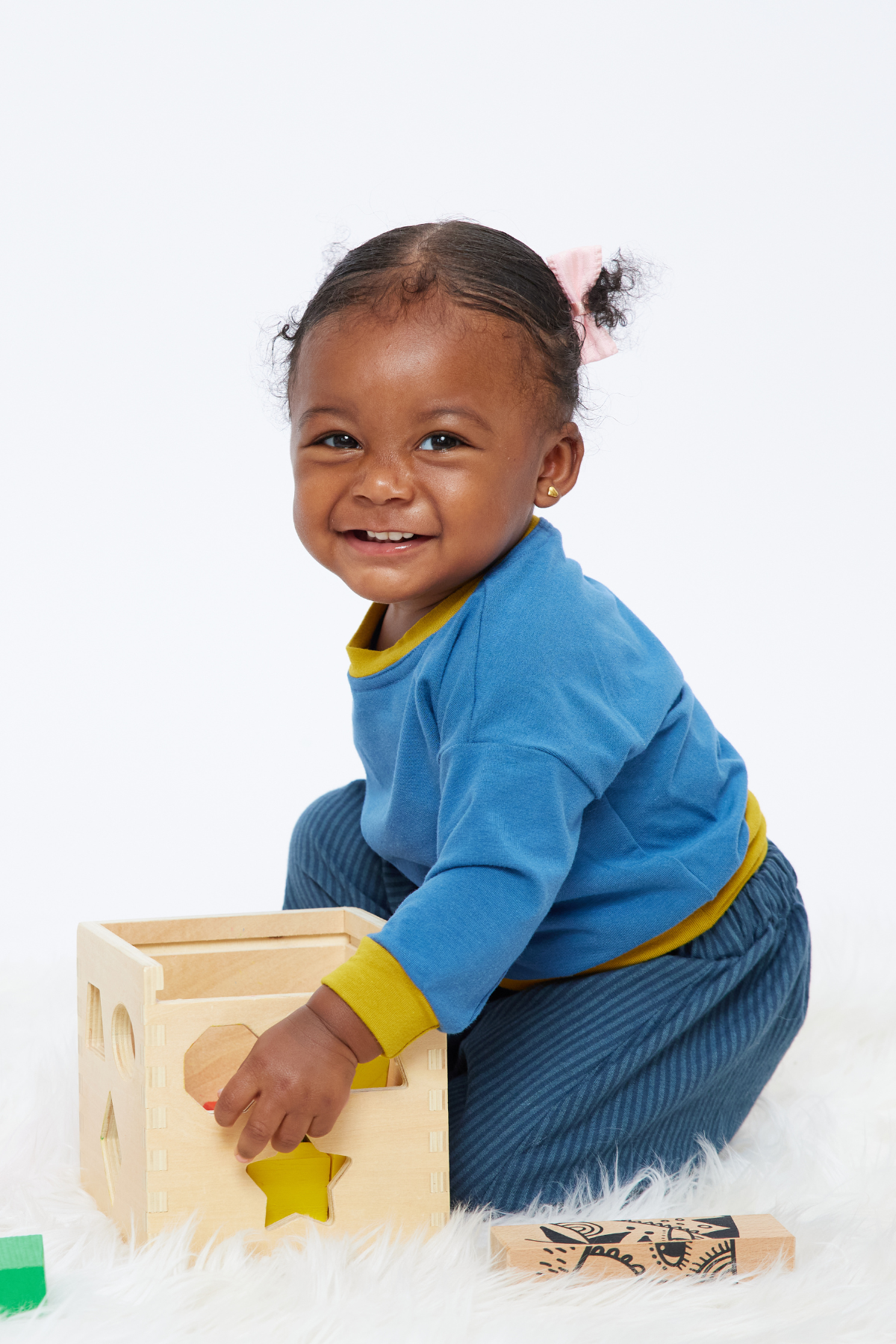 smiling baby playing with blocks wearing a gender-neutral blue and yellow pullover top