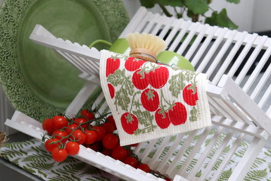 Kitchen towel with tomato pattern on a white dish rack with green plates and red tomatoes.