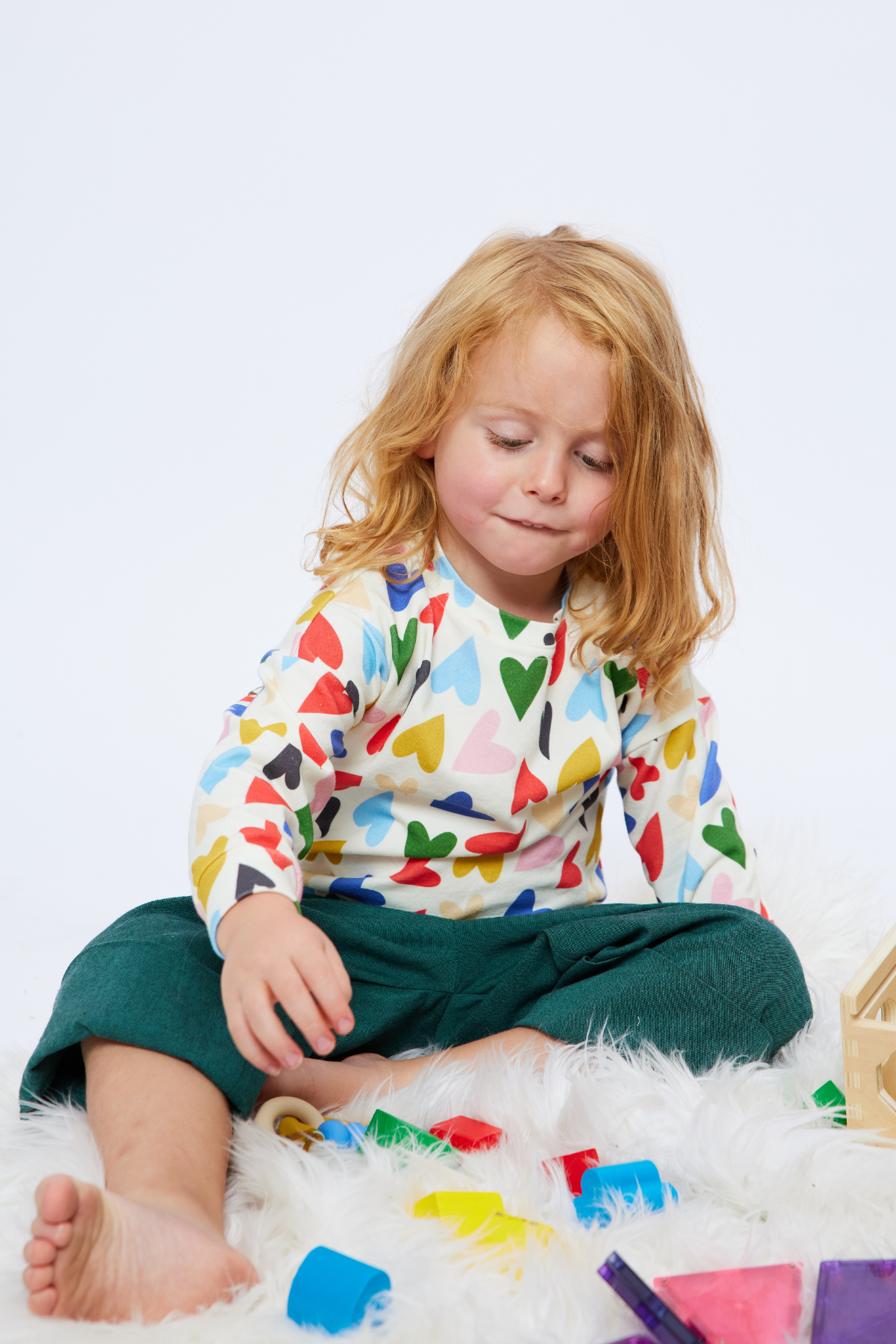 boy with long hair playing with blocks wearing an organic cotton top with colorful hearts