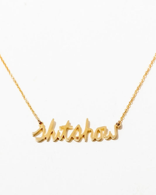 A gold-plated necklace with the phrase 'Shitshow' written in cursive script on a white background.
