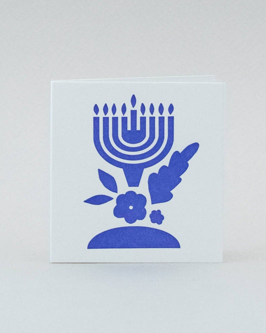 A folded mini card with a blue print design featuring a Hanukkah menorah and decorative flowers on a white background.