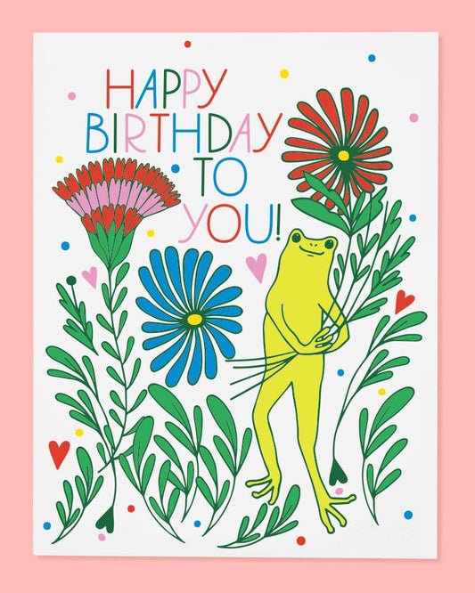 A colorful birthday card with an illustration of a frog holding a bouquet of flowers, with the text 'Happy Birthday to You!' on a bright pink background.