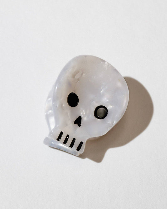 A small, skull-shaped hair clip made of cellulose acetate on a white background.