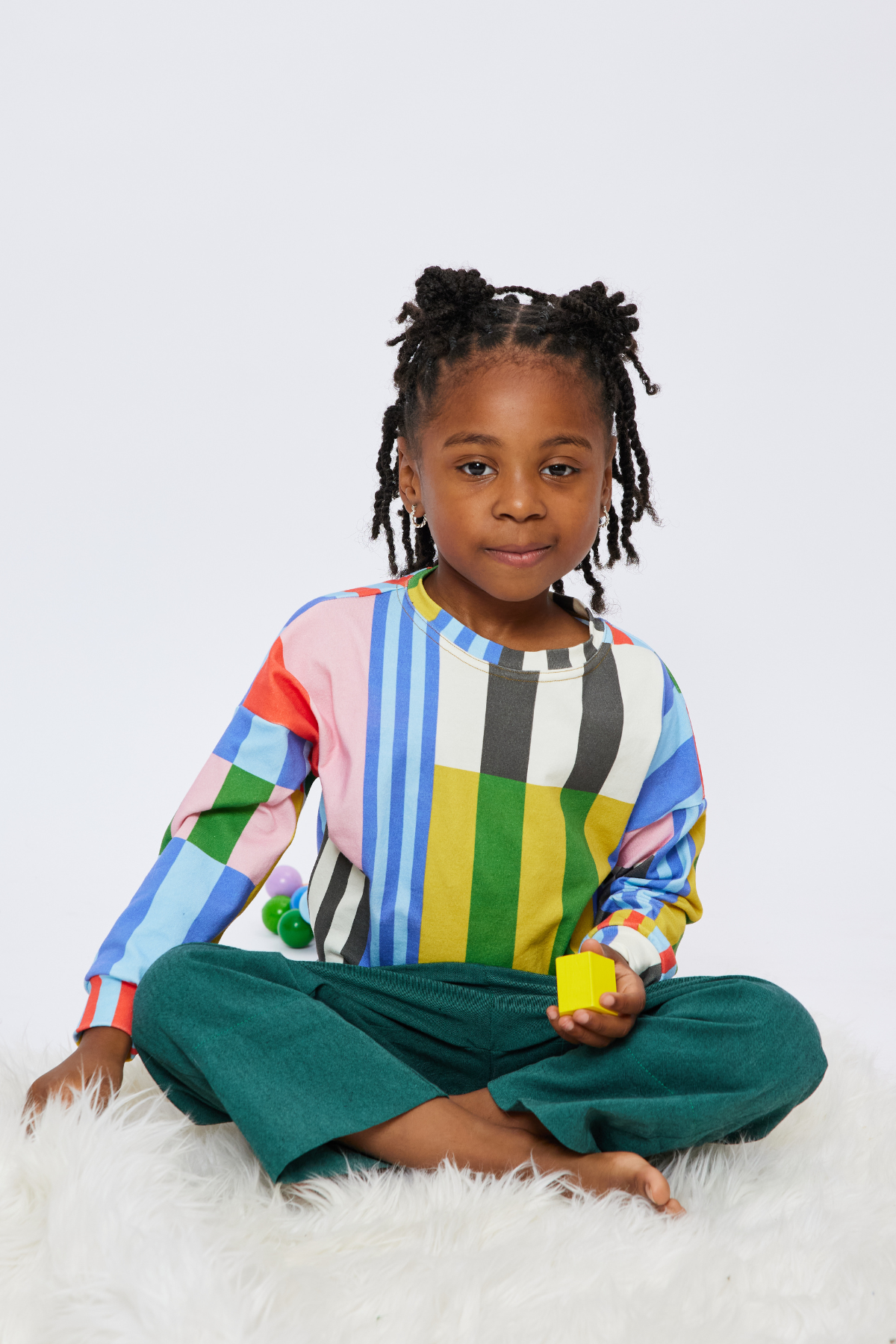 young kid sitting cross legged and wearing colorful kid clothes by Lilla Barn Clothing