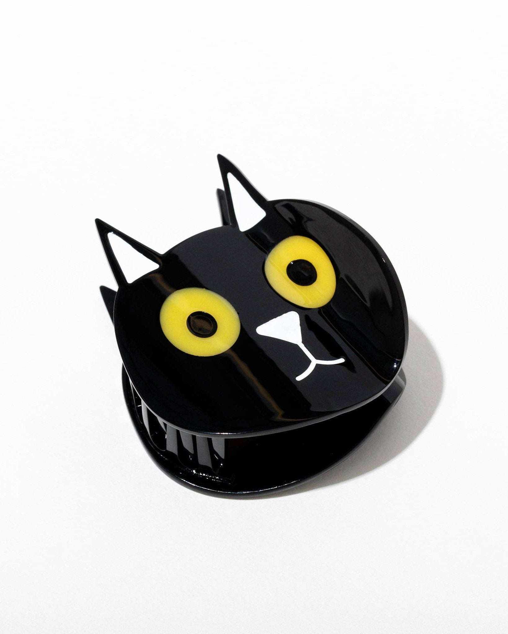 Black cat-shaped hair claw with yellow eyes and a white paws on a white background