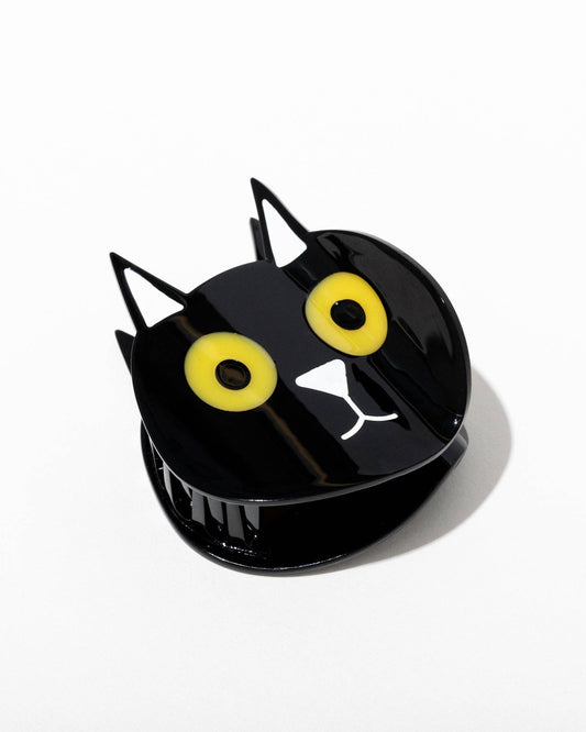 Black cat-shaped hair claw with yellow eyes and a white paws on a white background