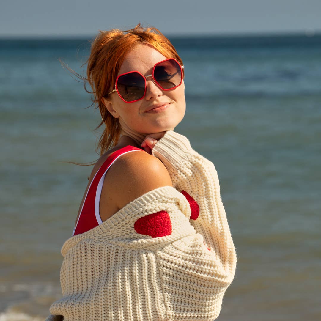 Woman on a beach wearing sunglasses and a red swimsuit with a white cover-up.