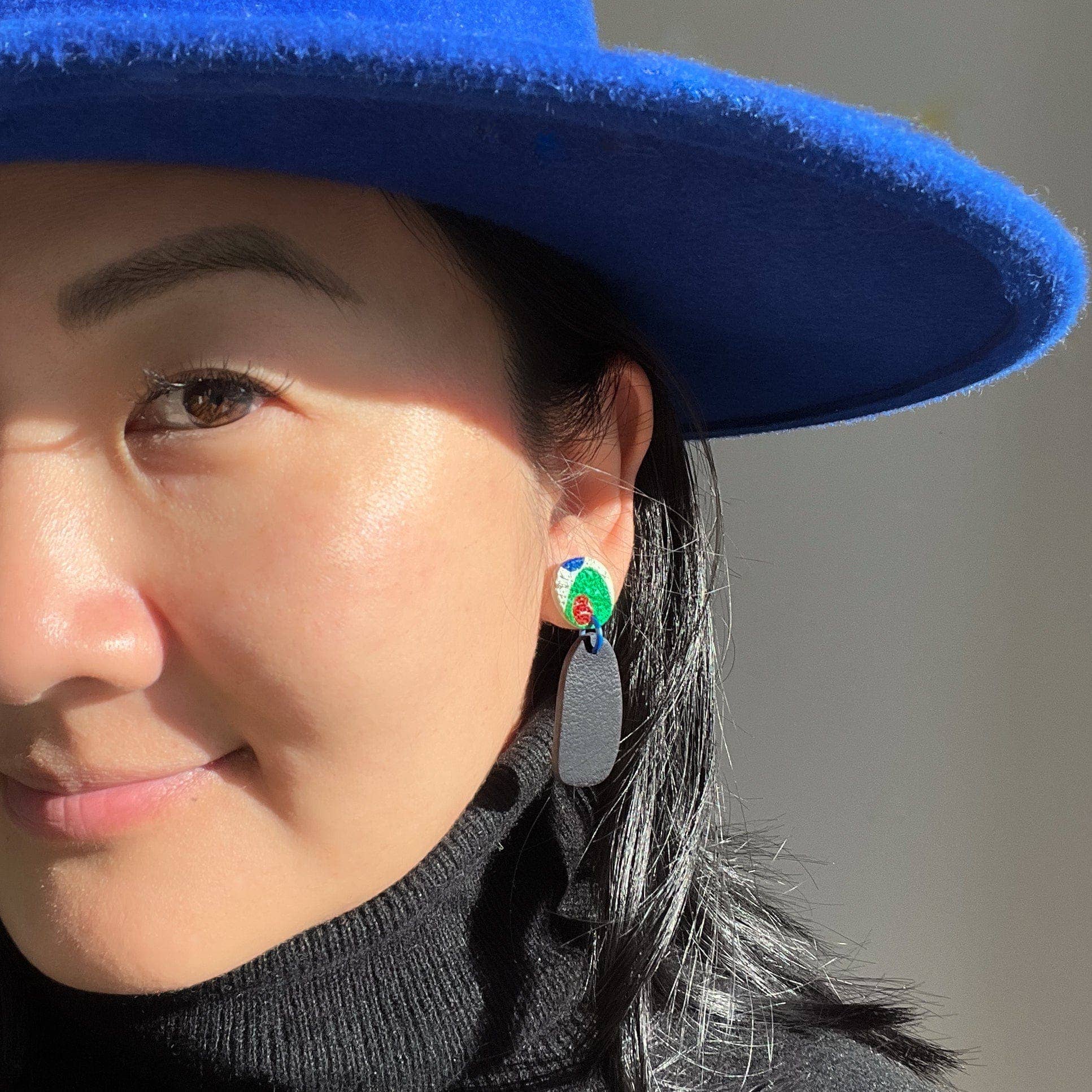 Close-up of a person wearing a blue hat and colorful earrings with a neutral background