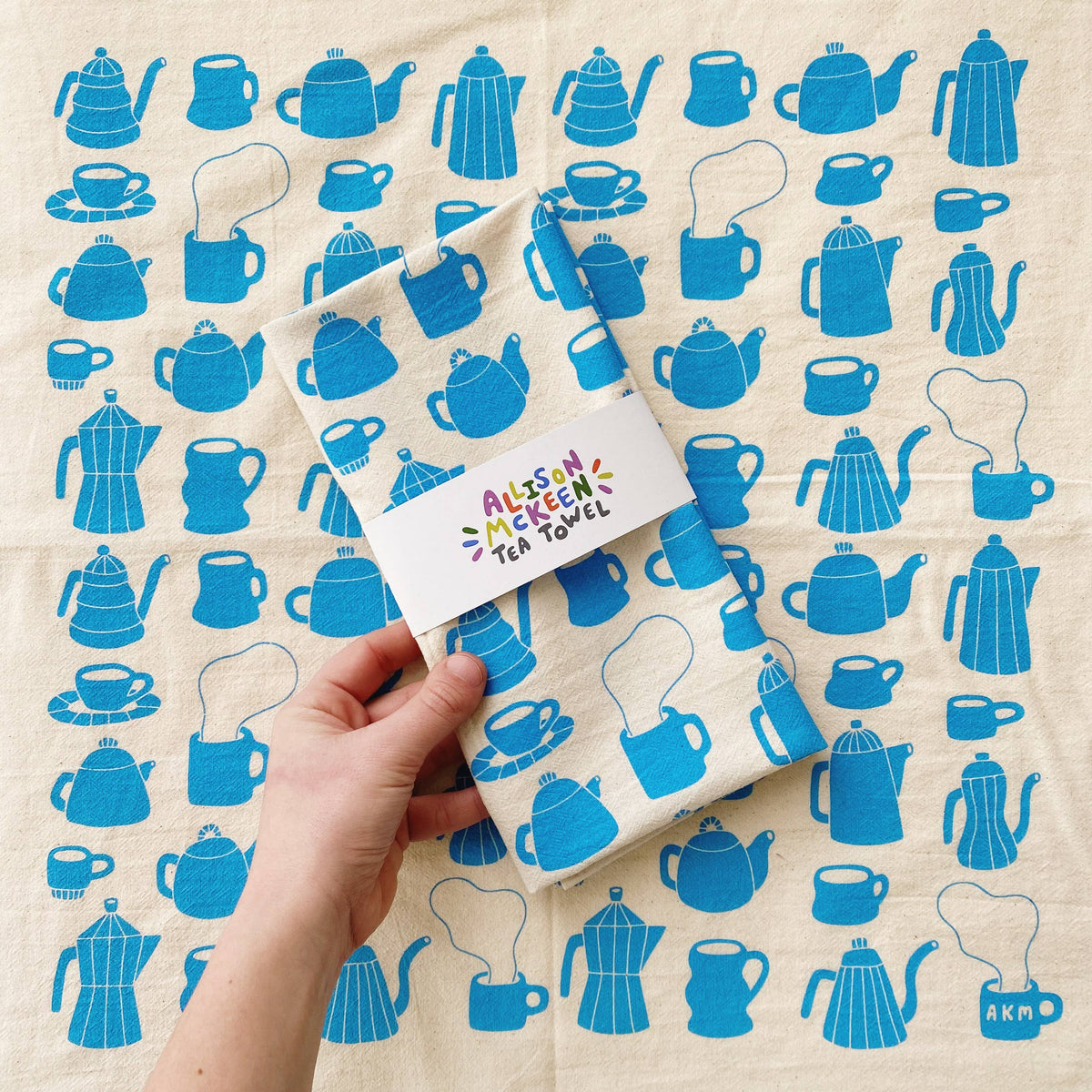 Tea towel with blue teapot pattern held by a hand on a matching background