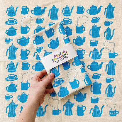 Tea towel with blue teapot pattern held by a hand on a matching background