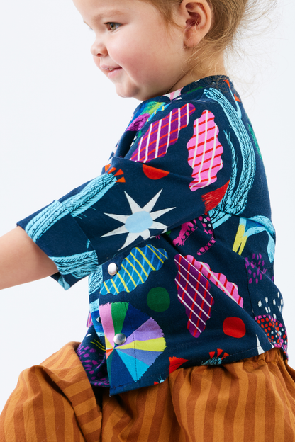 Child wearing a colorful kid shirt with abstract patterns and brown striped pants on a white background