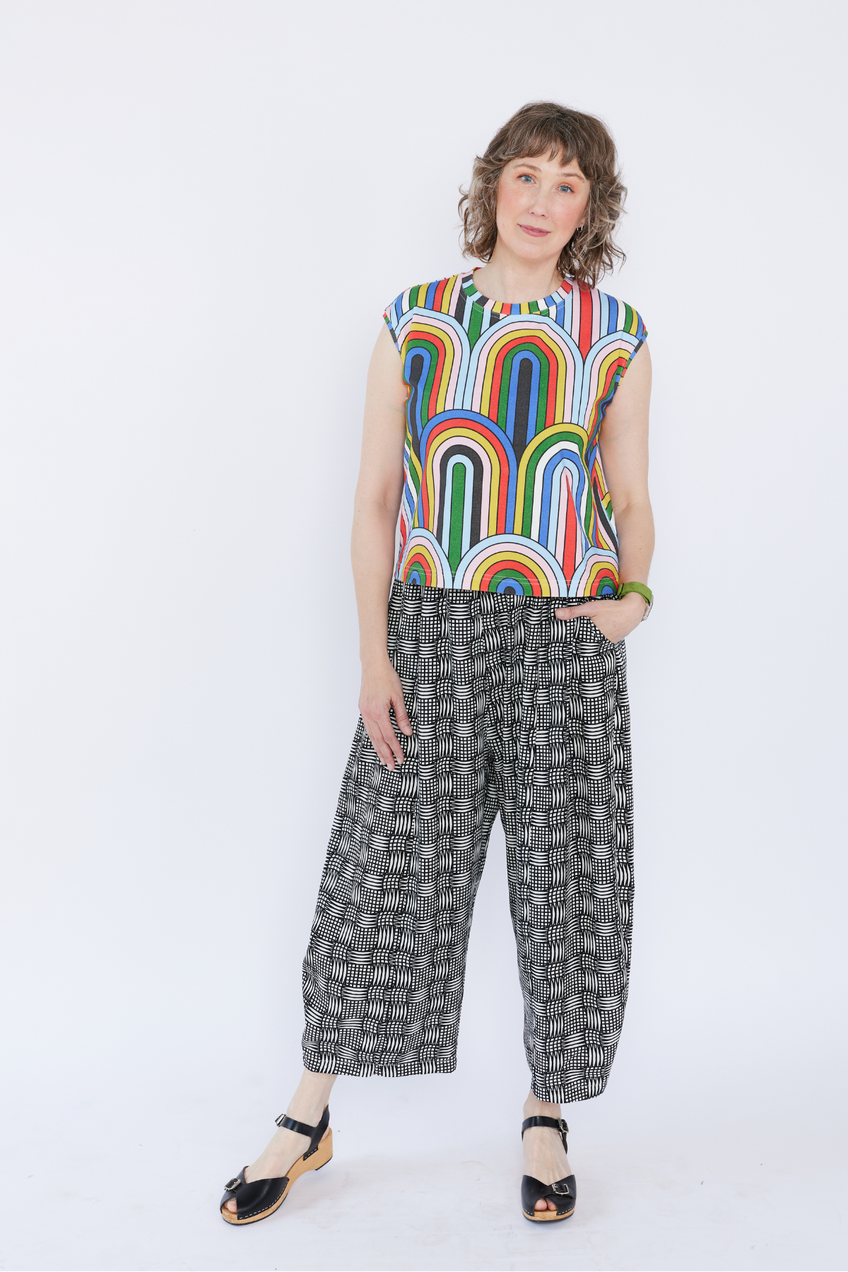 Woman wearing a colorful sleeveless top and patterned pants on a white background