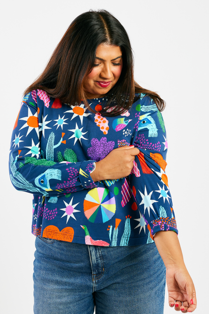 woman smiling and wearing a navy blue stretchy long-sleeve shirt with a colorful pattern. 