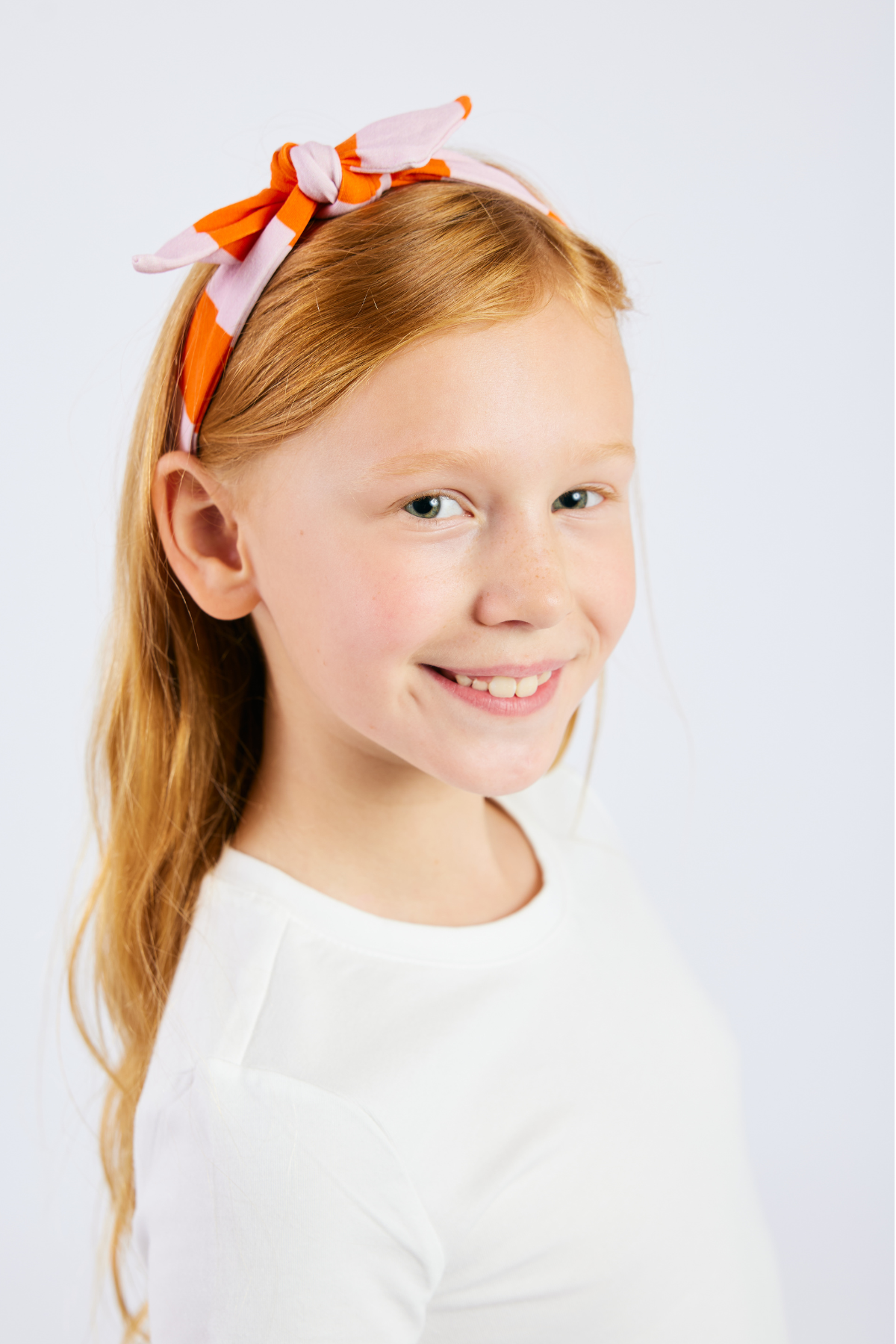child looking at camera and wearing a pink and orange striped stretchy headband