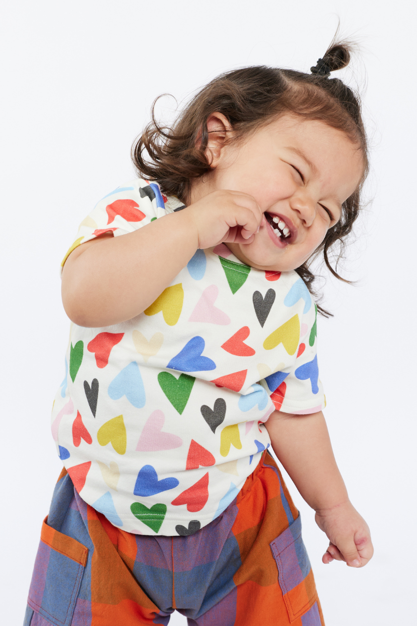 Child wearing a colorful shirt with heart patterns and checkered pants on a white background