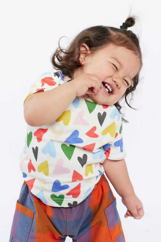 Child wearing a colorful shirt with heart patterns and checkered pants on a white background