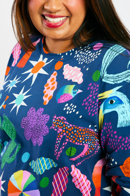 close up of a woman smiling and wearing a navy blue shirt with colorful animals and plants print