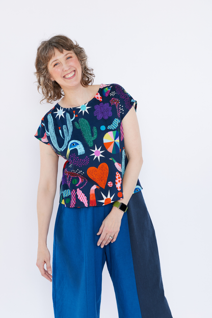 Woman wearing a colorful patterned top and blue pants against a white background