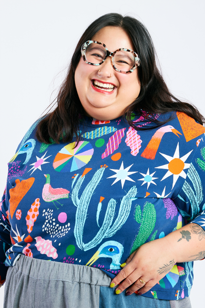Person laughing and wearing a sustainable plus size colorful patterned shirt with a plain background