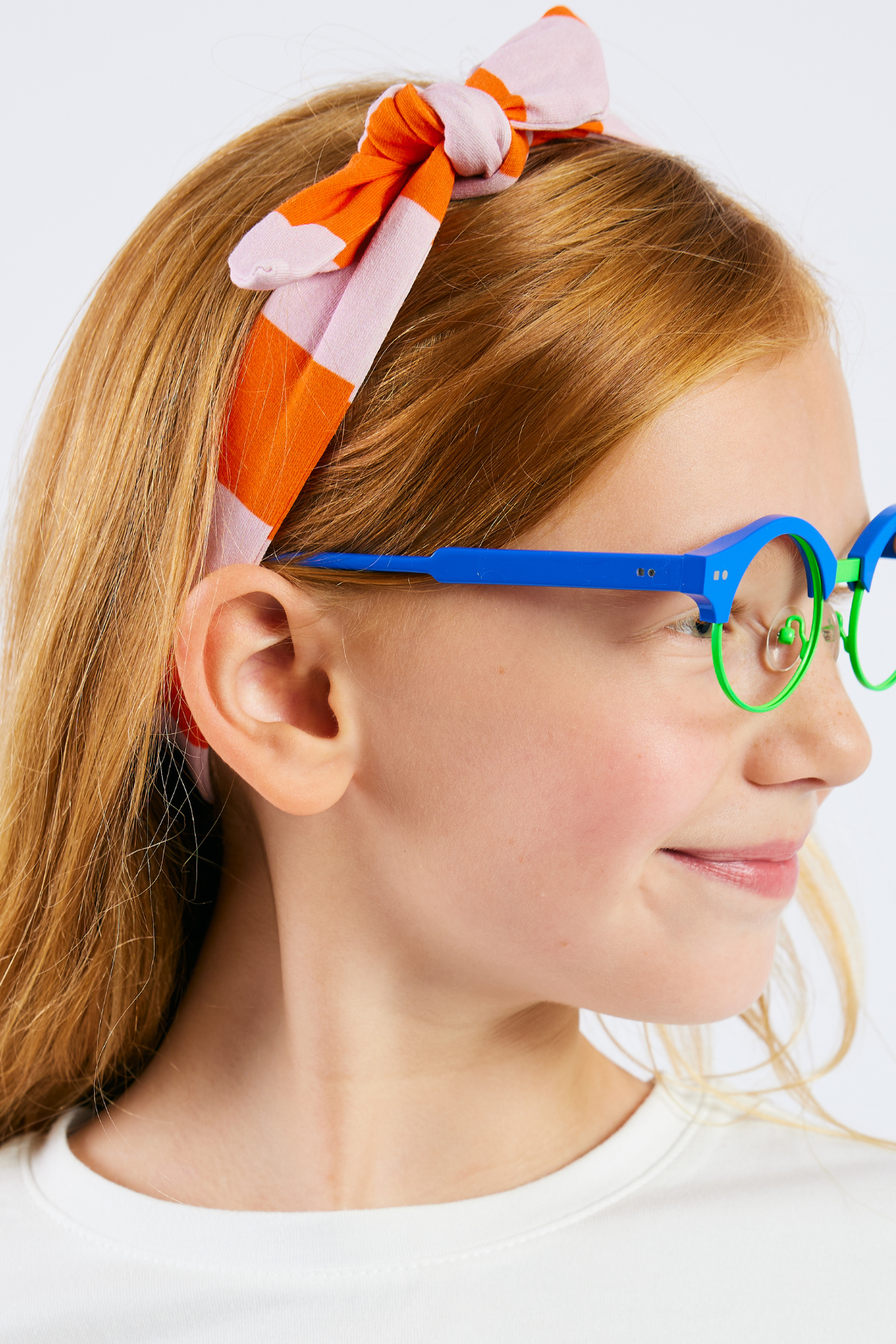 child wearing a pink and orange striped stretchy headband and bright blue glasses  from Eye Spy Optical