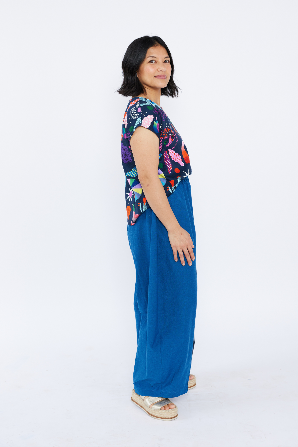 Woman wearing a colorful patterned top and blue pants on a white background