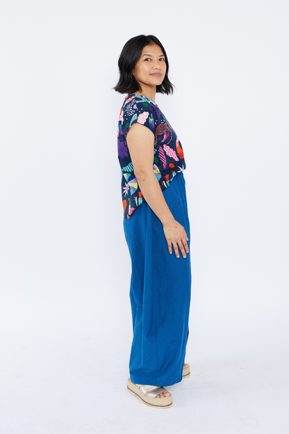 Woman wearing a colorful patterned top and blue pants on a white background