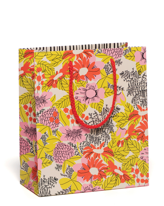 Floral patterned gift bag with a red handle on a white background