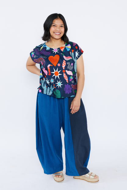 Woman wearing a colorful patterned top and blue pants on a white background