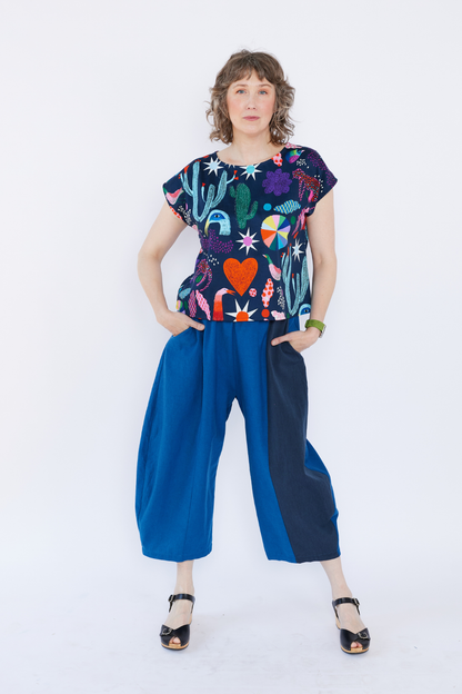 Woman wearing a colorful top with cactus and heart designs and blue pants on a white background
