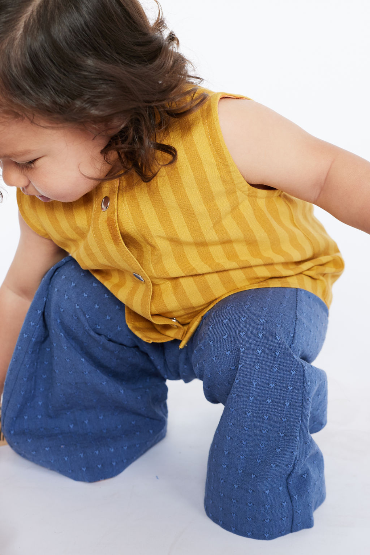 Child wearing a yellow striped shirt and blue pants on a white background