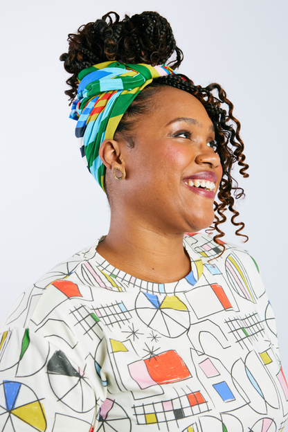 Woman wearing a colorful headscarf and patterned shirt against a white background