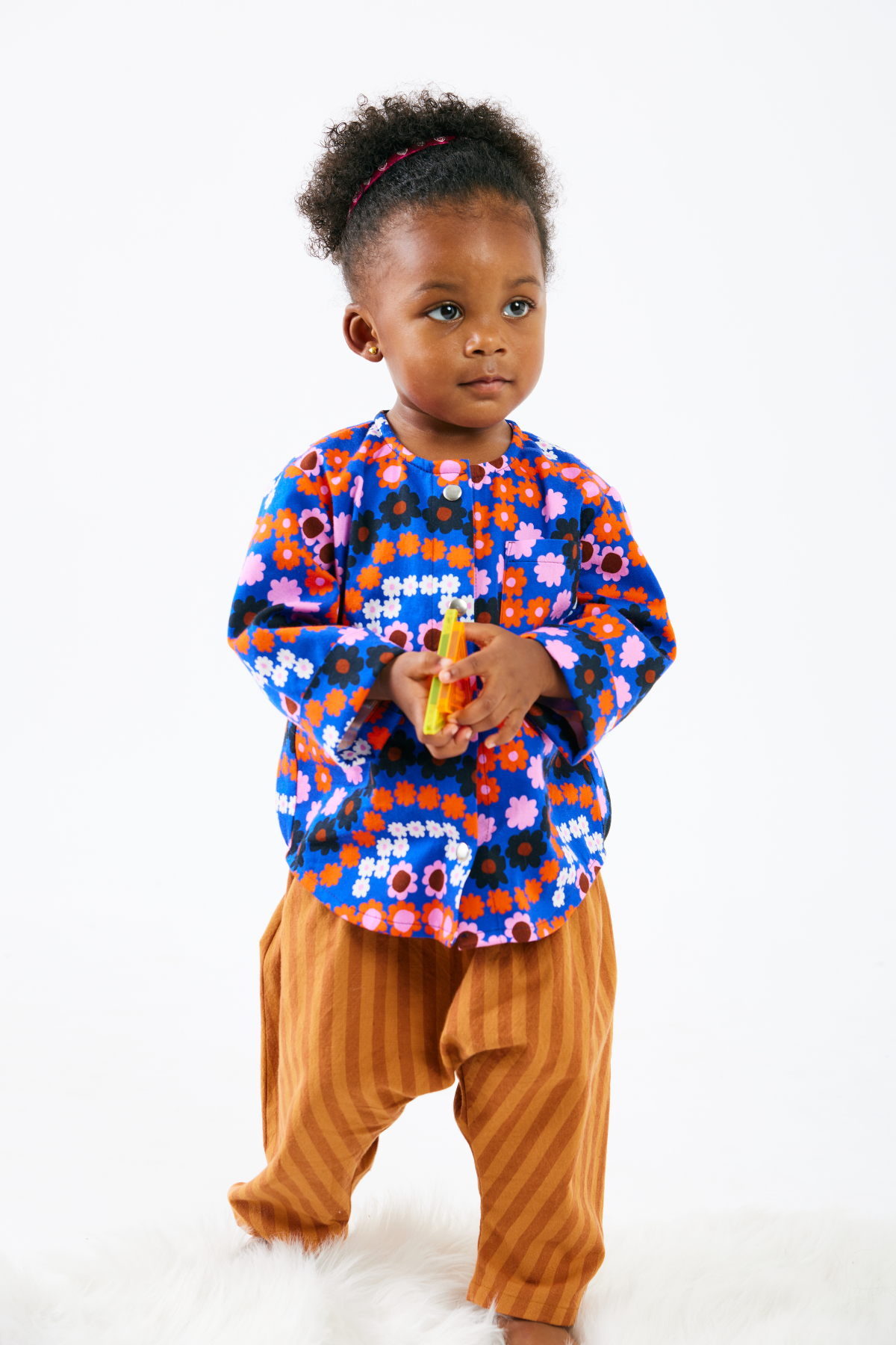 Child wearing a colorful floral top and brown pants on a white background