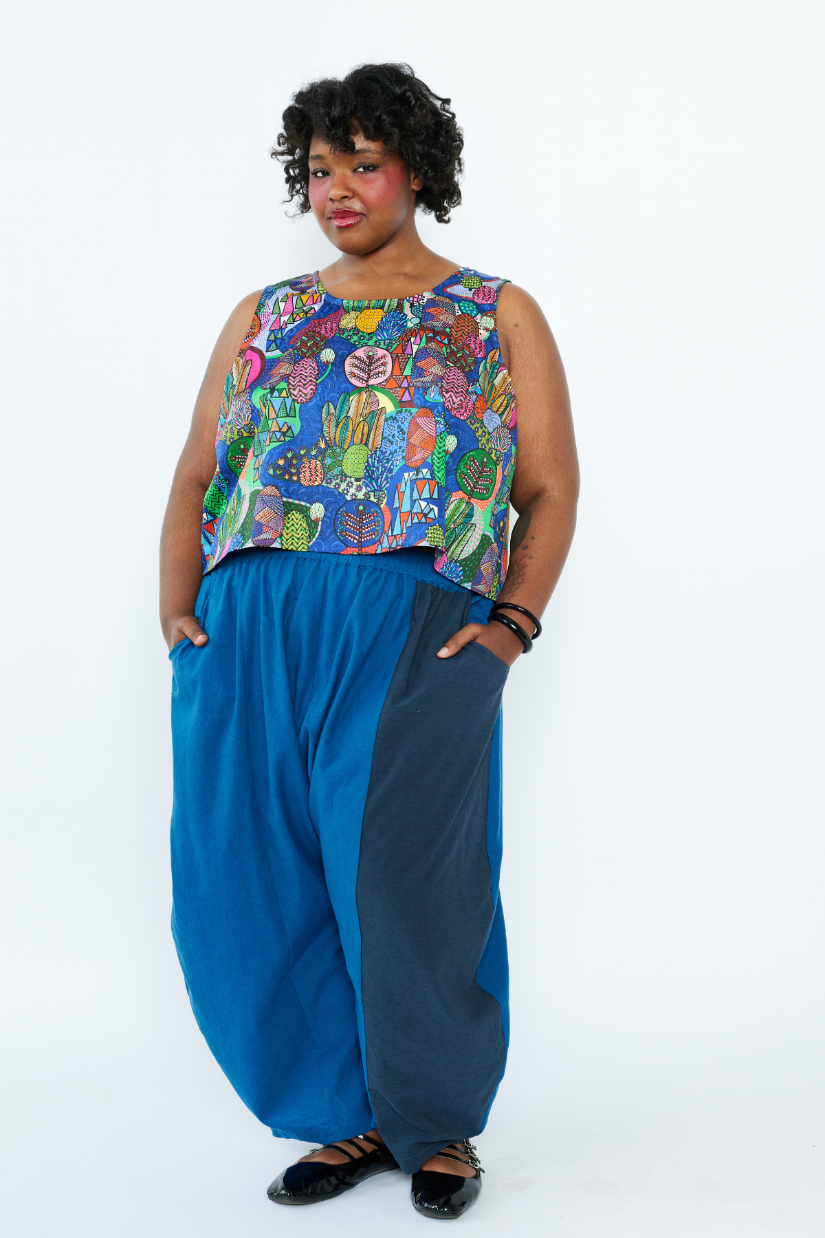 Woman wearing a colorful sleeveless top and blue pants on a white background
