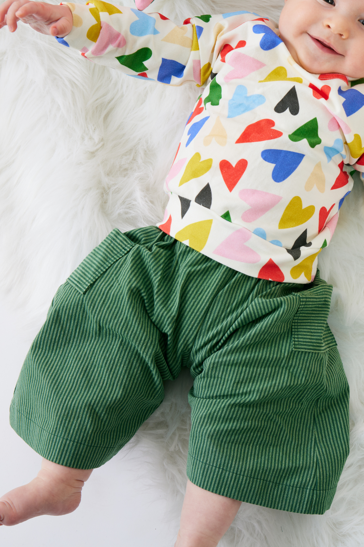 Baby wearing a colorful heart-patterned shirt and green pants on a white background