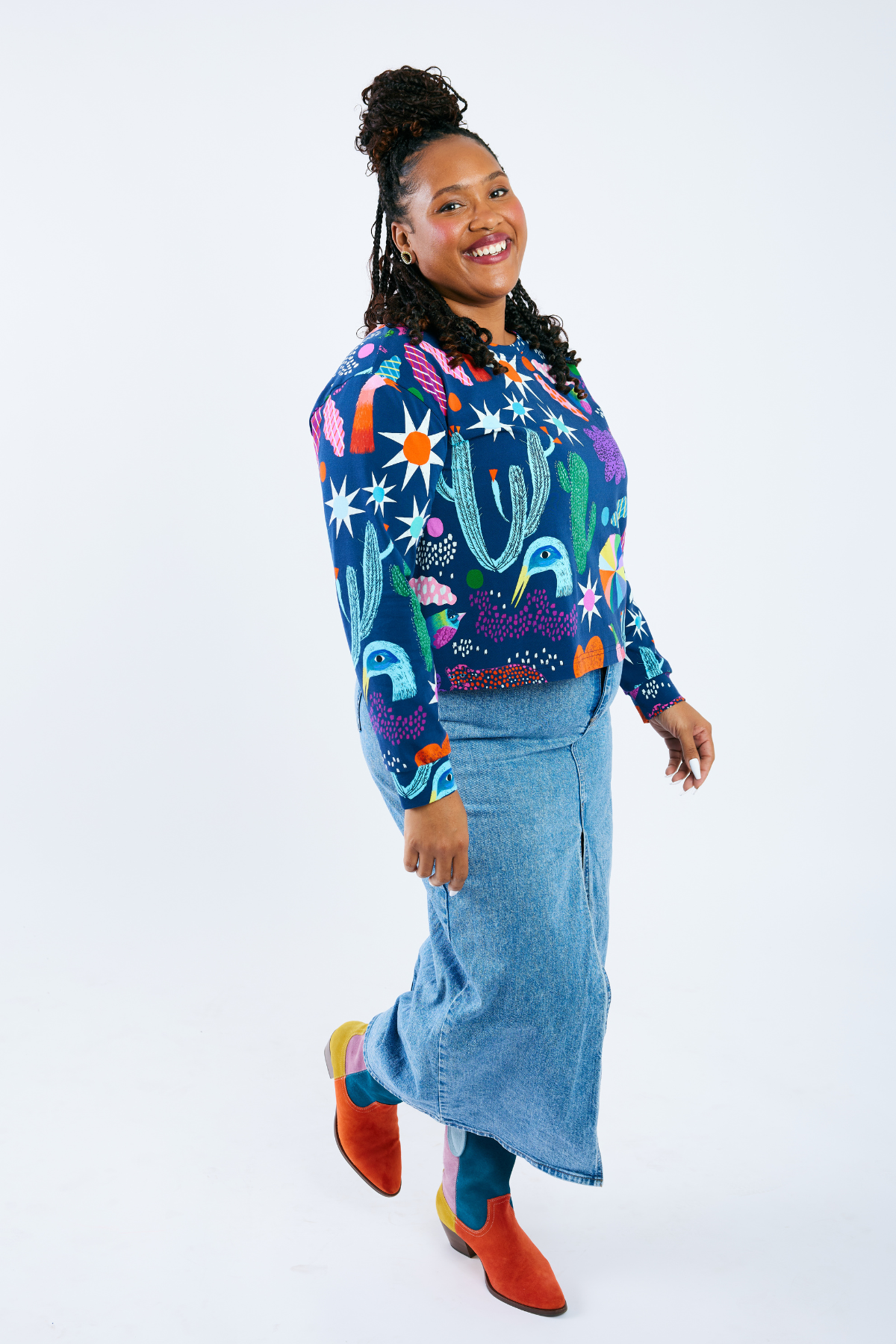 Woman wearing a colorful long sleeve shirt with cactus design and a blue skirt on a white background