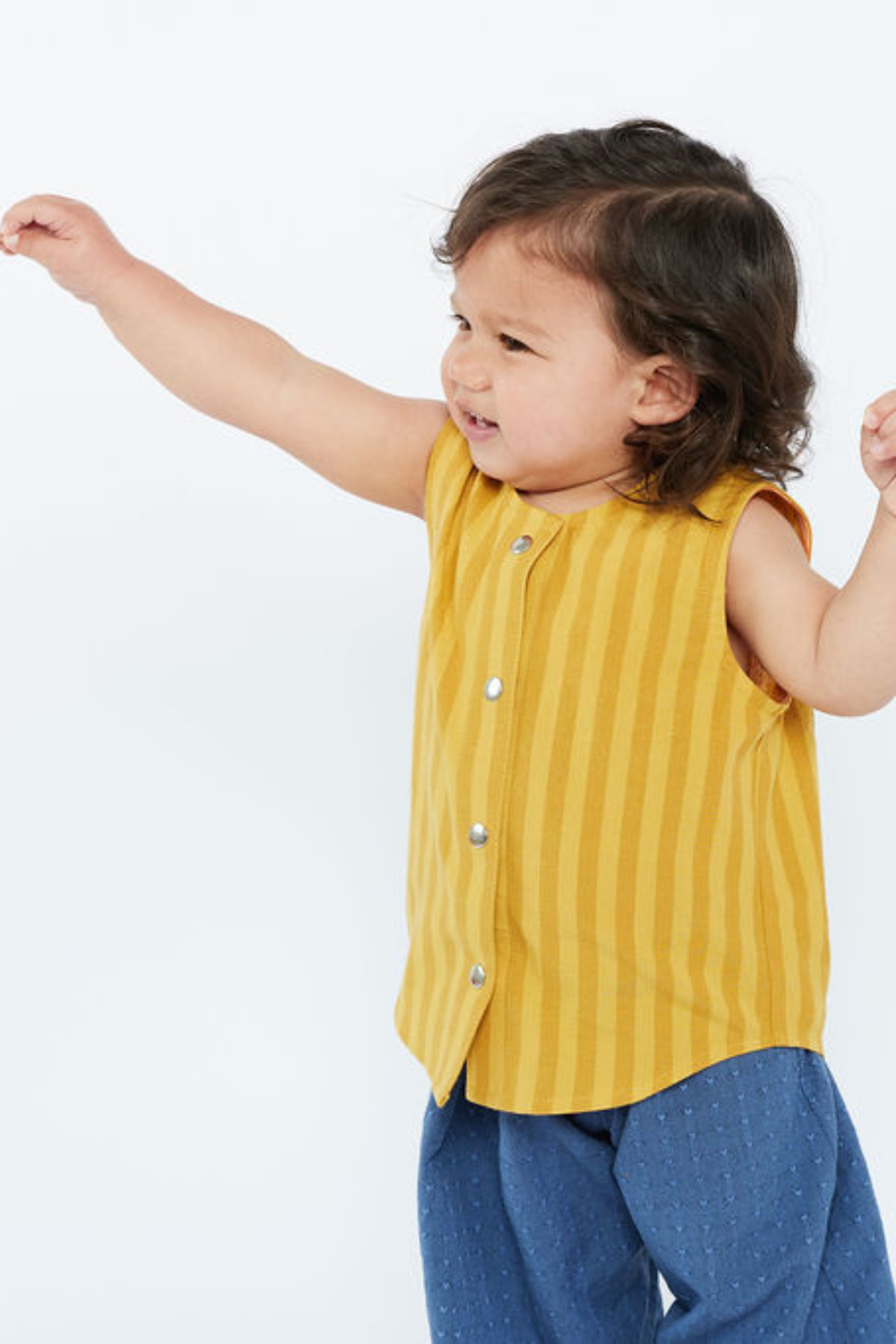 Child wearing a yellow sleeveless shirt with snaps and blue pants on a white background